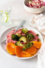 A wholesome breakfast with beet hummus, baked sweet potato, and a fresh radish and cabbage salad, rich in vitamins, fiber, and protein