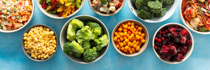 A variety of fresh vegetables frozen for winter, arranged on plates against a cool blue background,...
