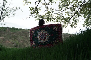 A young girl in an open field showcasing a beautifully handcrafted Kashmiri carpet, highlighting...