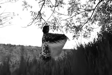 Black and white photograph of a girl holding an abstract-patterned carpet in wide open fields,...