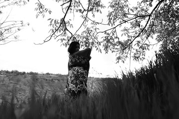 Black and white photograph of a girl holding an abstract-patterned carpet in wide open fields,...