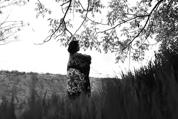 Black and white photograph of a girl holding an abstract-patterned carpet in wide open fields,...
