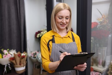 Business owner with clipboard taking notes in her flower shop, space for text