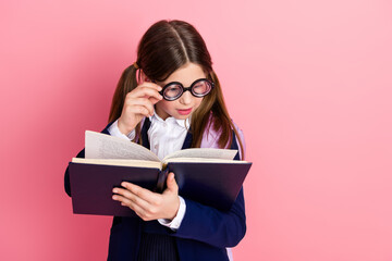 Young schoolgirl in formal uniform holding an open book with a curious and focused expression...