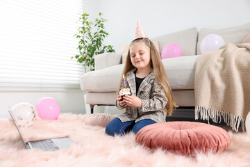 Birthday celebration. Little girl with cupcake having video call via laptop at home