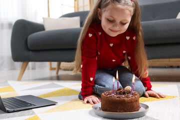 Birthday celebration. Little girl with cake having video call via laptop at home