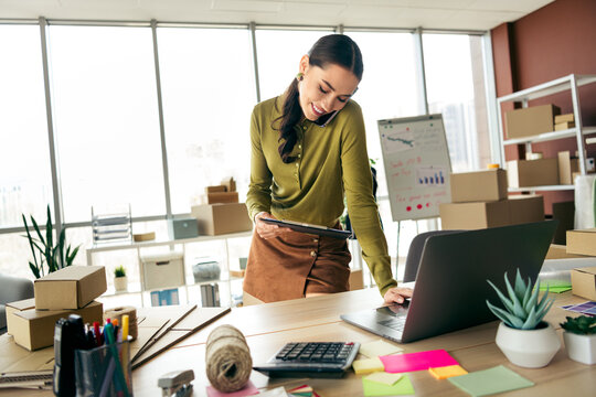 Young female entrepreneur managing online fashion business while multitasking in modern workplace with trendy interior