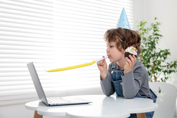 Little boy celebrating his birthday while having video call via laptop at table indoors. Space for...