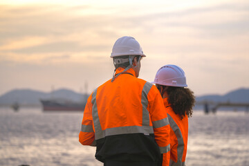 Two engineers wearing safety uniforms and hard hats communicate using a radio while reviewing data...