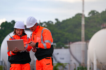 Two engineers in high-visibility safety gear and hard hats discuss project plans on a laptop in...