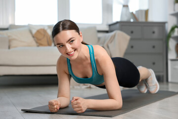 Obraz premium Smiling woman in sportswear doing plank exercise at home
