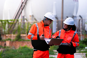 Two engineers in high-visibility safety gear and hard hats discuss project plans on a laptop in...