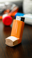 Orange Asthma Inhaler Standing on Wooden Table with Blurred Background