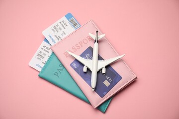 Passports with tickets, credit card and airplane model on pink background, top view