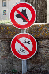 Sign that says no dog and no bikes. The sign is red and white. There is a tree behind the sign
