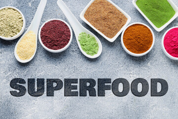 Superfood. Different powders in bowls and spoons on grey table, flat lay