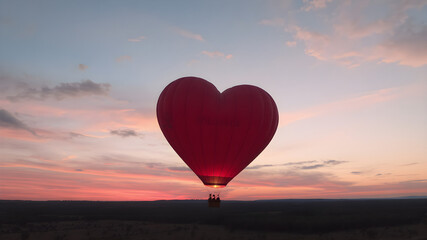Fototapeta premium A heart-shaped hot air balloon floating in the air, with a sunset sky as the backdrop, warm and soft colors