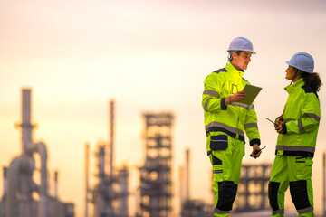 Two engineers in high-visibility safety gear and helmets conduct a field inspection at an...