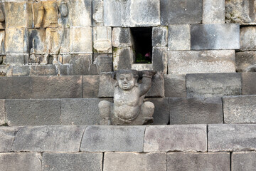 A stone guardian figure supports the temple structure at Borobudur with arms raised.