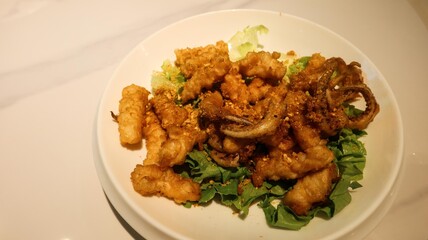 close up of Cantonese dish of deep fried salt and pepper squid  with garlic on a white plate