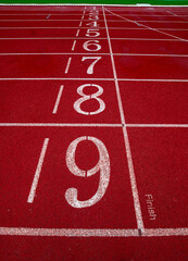 Close up of red synthetic running track finish line with lane numbers 1–9 , symbolizing sports ,...
