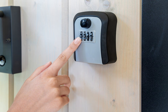 Hand Entering Code on Wall-Mounted Lockbox. Close-up of a person entering a numeric code on a combination key lockbox mounted to a wooden wall for secure access.