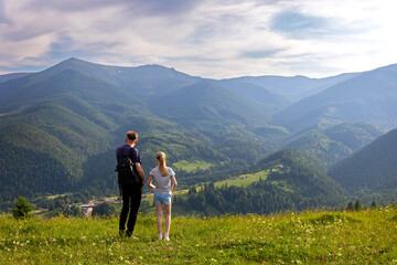 Father and Daughter Admiring Mountain Valley View. Man and young girl standing on a grassy hilltop,...