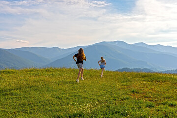 Two Girls Running on Sunny Mountain Hill. Back view of two girls running uphill on a sunlit meadow...