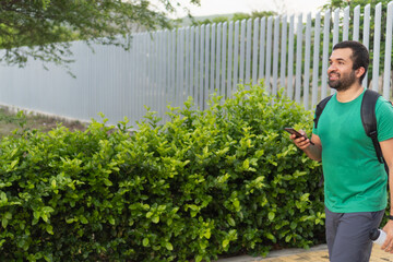 Man walking outdoors holding smartphone and water bottle after workout