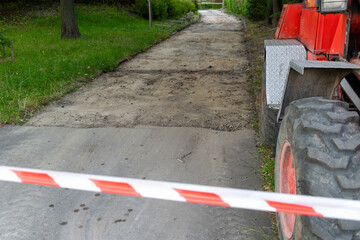Construction zone with red tractor and caution tape on dirt road