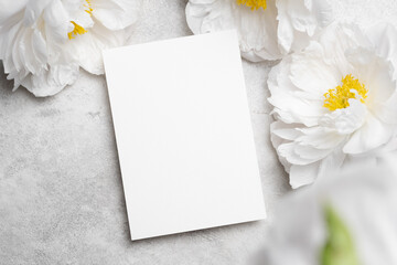 Blank invitation, flyer or greeting card mockup with copy space and peony flowers on stony...