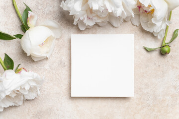 White square mock up with copy space surrounded by fresh peony flowers on a textured beige...