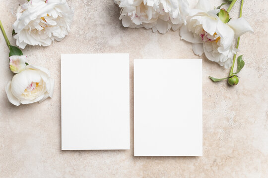Two blank wedding invitation cards mockup with copy space for card design presentation, white cards with peony flowers on beige concrete background