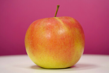 Ripe red yellow fresh apple on pink background, close-up