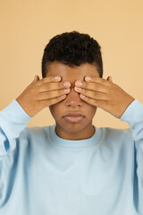 Vertical image of a dark skinned Latino teenager wearing a pastel blue sweatshirt, covering his...