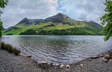 A cloudy day at Buttermere Lake, with gentle waves rippling across the wind-blown water, set...