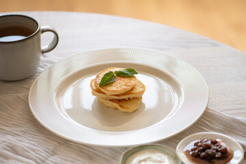 Small cheese pancakes decorated with mint leaves served with sour cream and jam on white table with tea for breakfast