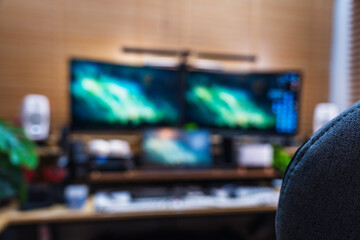 Modern home office setup with ergonomic gray chair, multi-monitor screens, wood desk, and green plants, creating a productive and stylish workspace environment.