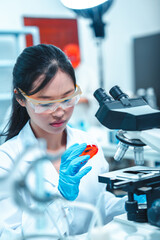 Confident female scientist in lab coat using microscope to analyze sample in petri dish. Concept of...