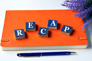 RECAP - a word written on wooden cubes on an orange notepad with a pen lying nearby