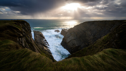 Naklejka premium Sunlight streams through storm clouds over the rugged irish coastline