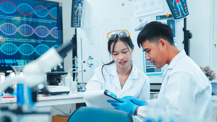 Two young scientists in lab coats and gloves discussing research results in laboratory....