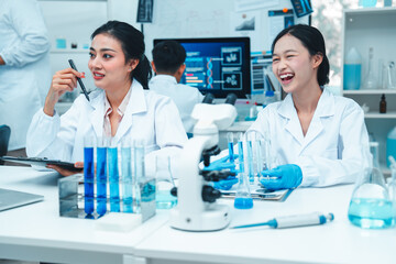 Two female scientists in lab coats working together in a science laboratory. One takes notes on a...