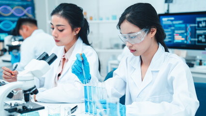 Two female scientists working in a modern laboratory. One is carefully transferring liquid with a...