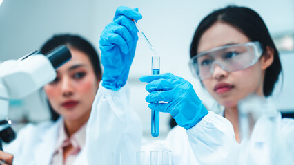 Two female scientists working in a modern laboratory. One is carefully transferring liquid with a...