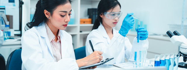 Two female scientists working in a modern laboratory. One is carefully transferring liquid with a...