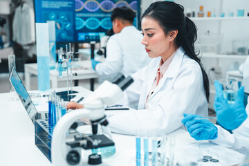 Two female scientists analyzing test tube samples in a laboratory setting. One supervises while the...
