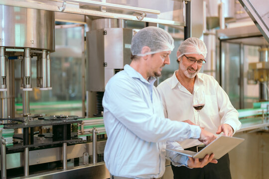 Two professionals discuss quality control in a food processing plant during working hours while reviewing data on a laptop