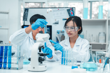 Two scientists in a laboratory working with test tubes. holds up a blue liquid sample while the...