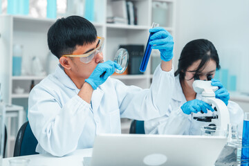 Two scientists in a laboratory working with test tubes. holds up a blue liquid sample while the...